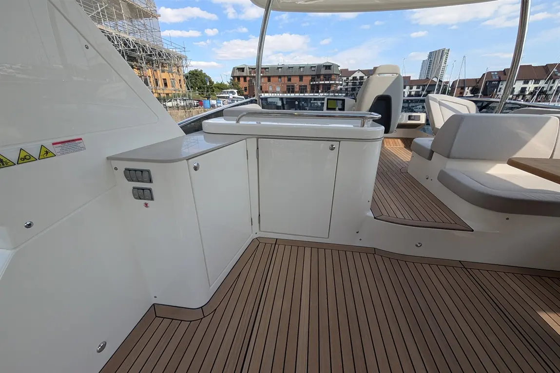 Modern yacht interior with a polished surface, seating area, control panel, and scenic marina view under a blue sky.